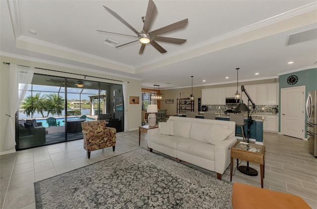 living room with ceiling fan, visible vents, and a raised ceiling