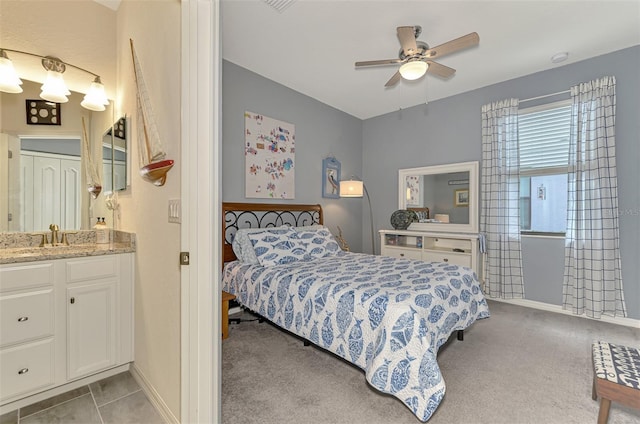 bedroom featuring ensuite bathroom, light colored carpet, a sink, a ceiling fan, and baseboards