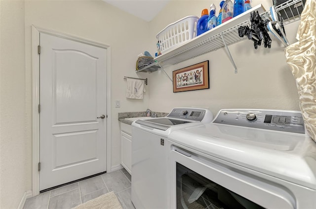 washroom with cabinet space, baseboards, separate washer and dryer, and a sink