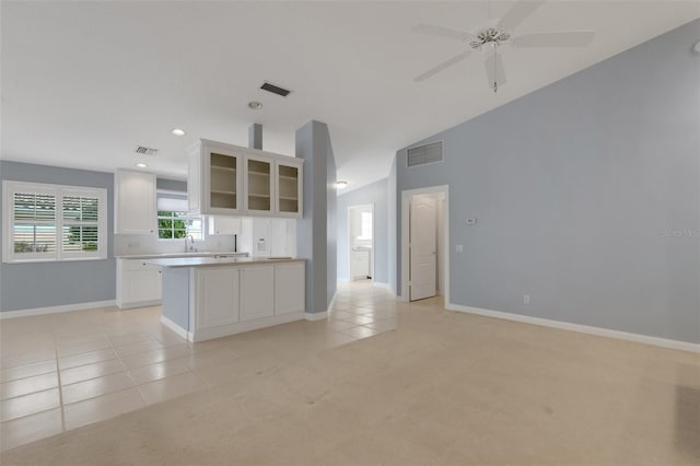 kitchen featuring light tile patterned floors, visible vents, light colored carpet, glass insert cabinets, and vaulted ceiling