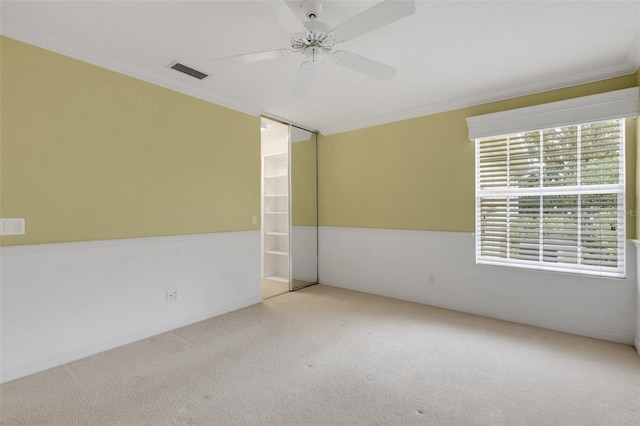 carpeted empty room featuring ornamental molding, visible vents, and a ceiling fan