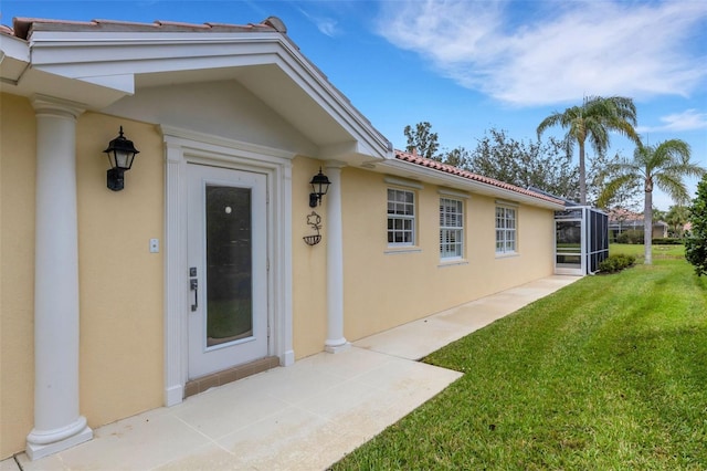 view of exterior entry featuring a lawn and stucco siding