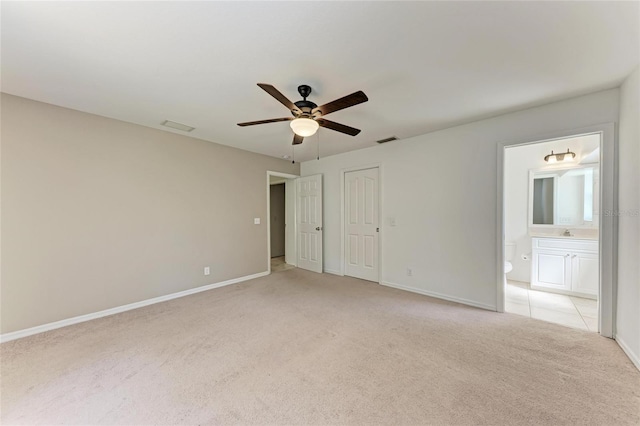 unfurnished bedroom featuring baseboards, ensuite bathroom, a ceiling fan, and light colored carpet