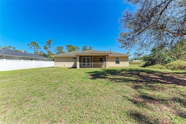 rear view of house with stucco siding, fence, and a yard