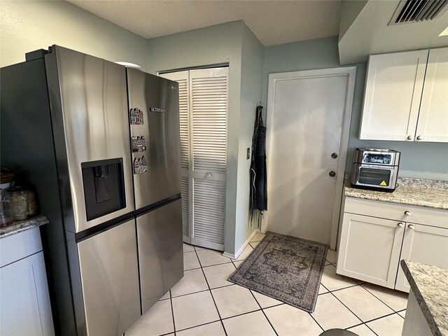1805 Springwood Dr, Sarasota, FL 34232 - kitchen with stainless steel fridge, white cabinets, light tile patterned flooring, and light stone countertops