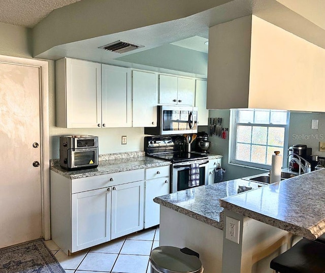 1805 Springwood Dr, Sarasota, FL 34232 - kitchen featuring stainless steel appliances, white cabinets, light tile patterned floors, a sink, and a kitchen bar