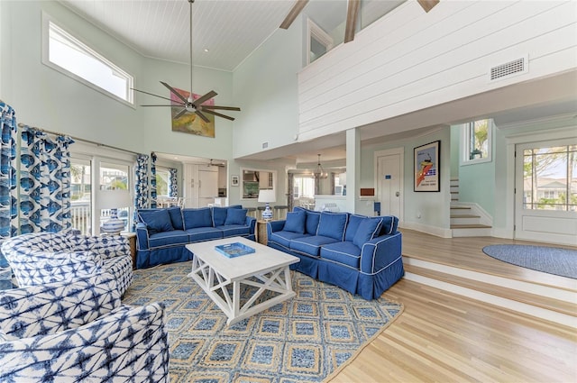 living room featuring ceiling fan with notable chandelier, wood finished floors, visible vents, baseboards, and stairway