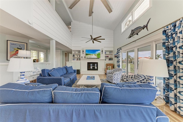 living area with ceiling fan, high vaulted ceiling, a brick fireplace, and wood finished floors