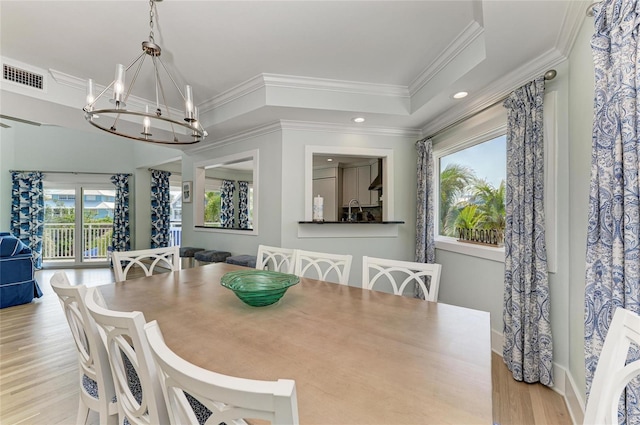 dining area featuring a notable chandelier, visible vents, light wood-style floors, ornamental molding, and a tray ceiling