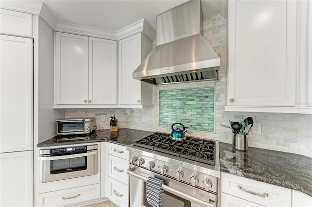 kitchen with a toaster, decorative backsplash, appliances with stainless steel finishes, wall chimney range hood, and dark stone countertops