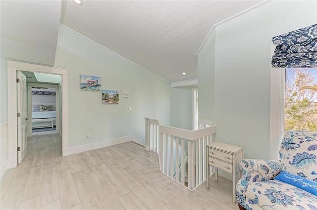 hallway with baseboards, vaulted ceiling, light wood-style flooring, and an upstairs landing