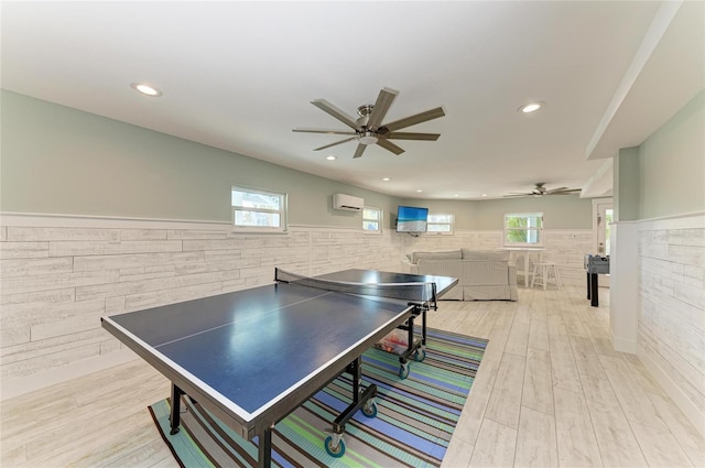 playroom featuring a ceiling fan, a wainscoted wall, an AC wall unit, light wood-type flooring, and recessed lighting