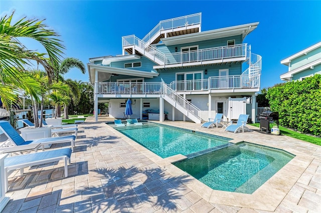 rear view of property featuring a patio, a pool with connected hot tub, ceiling fan, a balcony, and stairs