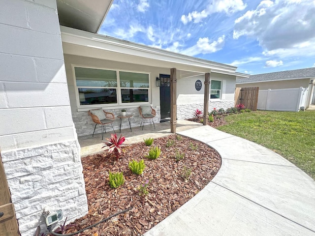 entrance to property with stone siding, a porch, a lawn, and fence