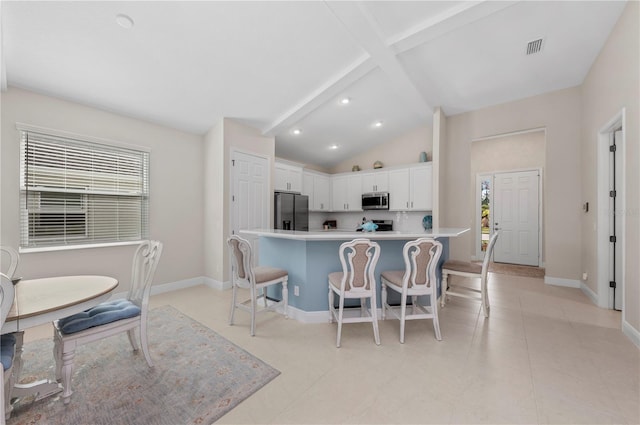 kitchen with lofted ceiling with beams, a breakfast bar, visible vents, white cabinets, and appliances with stainless steel finishes