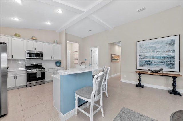 kitchen with light countertops, backsplash, lofted ceiling with beams, appliances with stainless steel finishes, and white cabinetry