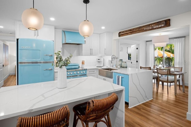 kitchen featuring a peninsula, a sink, stainless steel range with electric cooktop, custom range hood, and fridge