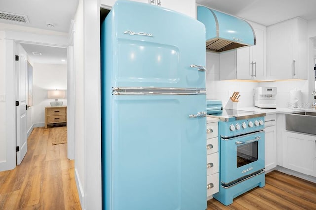 kitchen featuring premium range hood, light wood-style flooring, high end stainless steel range, and freestanding refrigerator