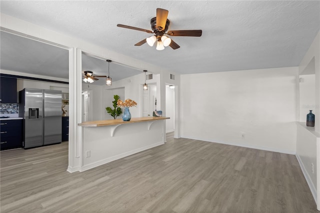 unfurnished living room featuring a ceiling fan, baseboards, light wood-style flooring, and a textured ceiling