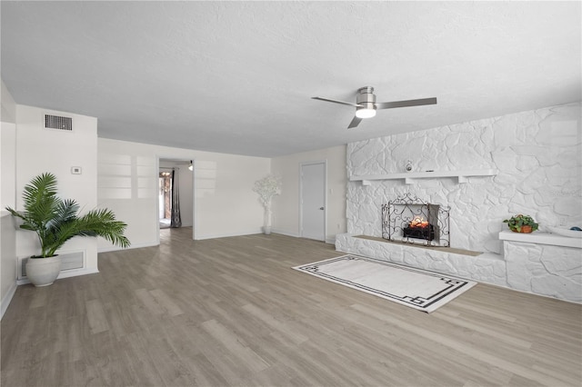 unfurnished living room with visible vents, a ceiling fan, wood finished floors, a textured ceiling, and a fireplace