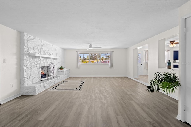 unfurnished living room with light wood-style floors, a fireplace, baseboards, and ceiling fan