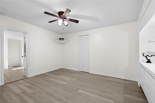 unfurnished room featuring a textured ceiling, ceiling fan, light wood-type flooring, and baseboards