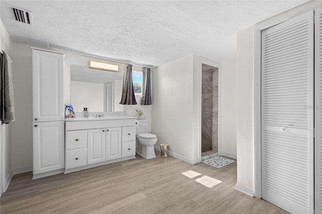 full bath with visible vents, toilet, a textured ceiling, wood finished floors, and tiled shower