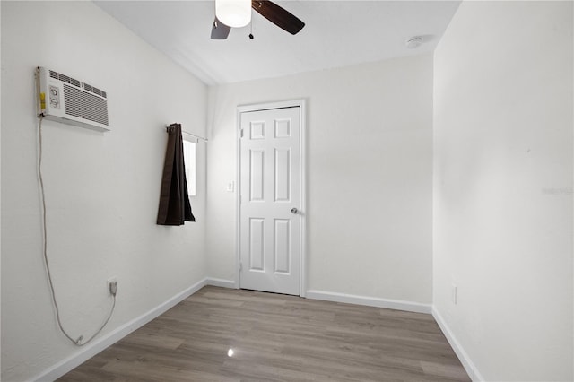 empty room with a ceiling fan, a wall mounted AC, baseboards, and wood finished floors