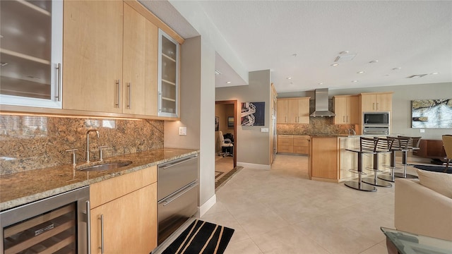 kitchen with light brown cabinetry, a sink, wine cooler, wall chimney range hood, and built in microwave