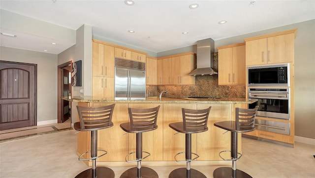 kitchen featuring a warming drawer, light brown cabinets, wall chimney range hood, decorative backsplash, and built in appliances