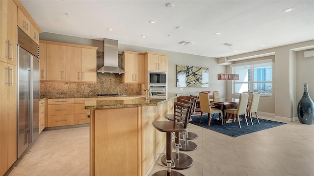 kitchen with visible vents, stone countertops, light brown cabinetry, built in appliances, and wall chimney range hood