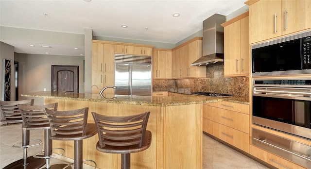 kitchen featuring a warming drawer, light tile patterned flooring, light brown cabinetry, built in appliances, and wall chimney range hood