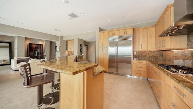 kitchen featuring light brown cabinets, visible vents, a sink, appliances with stainless steel finishes, and wall chimney exhaust hood