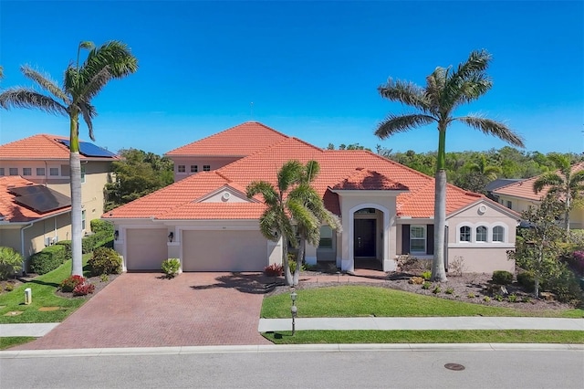 mediterranean / spanish-style house with a garage, a tile roof, decorative driveway, a front lawn, and stucco siding