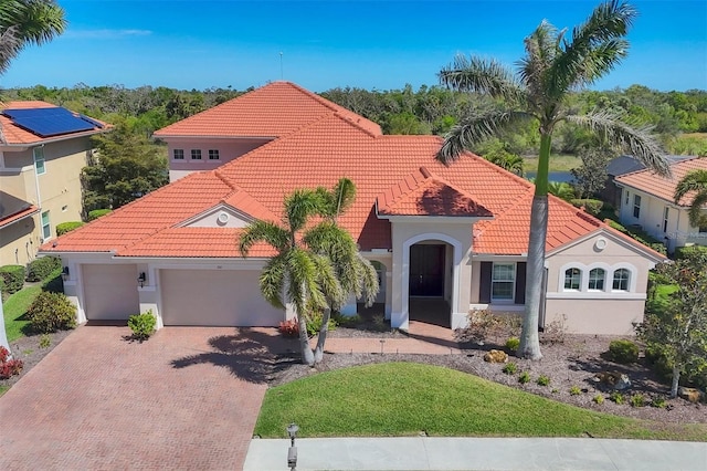 mediterranean / spanish-style house with decorative driveway, a tiled roof, an attached garage, and stucco siding