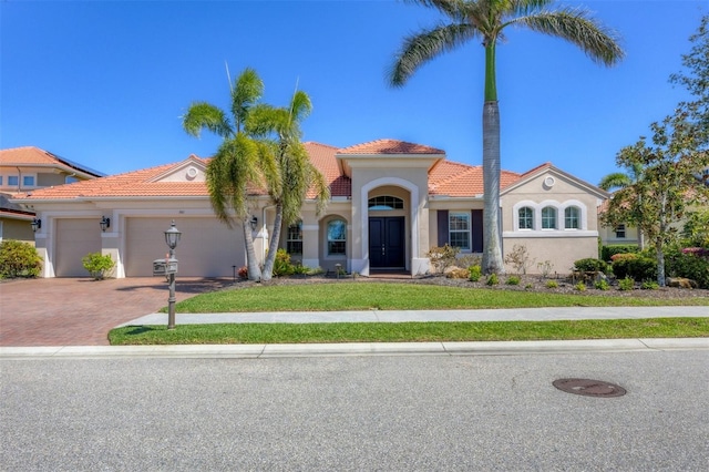 mediterranean / spanish home featuring decorative driveway, a tile roof, stucco siding, an attached garage, and a front yard