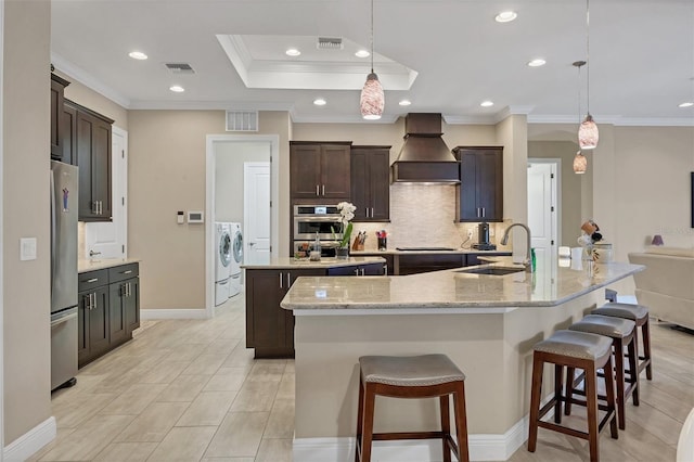 kitchen featuring a large island, custom range hood, freestanding refrigerator, a sink, and washer and dryer