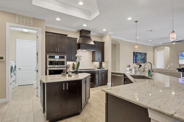 kitchen with a sink, appliances with stainless steel finishes, backsplash, a large island with sink, and custom range hood