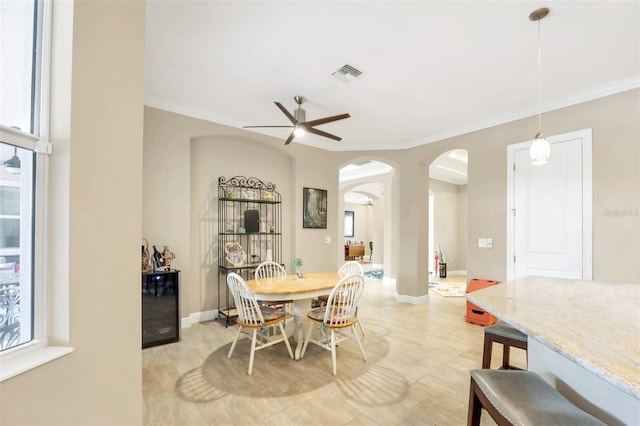 dining room with arched walkways, visible vents, baseboards, a ceiling fan, and ornamental molding