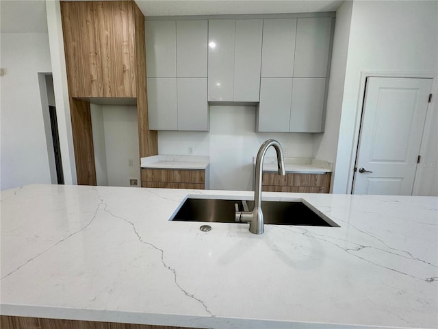 kitchen with light stone countertops, modern cabinets, gray cabinets, and a sink