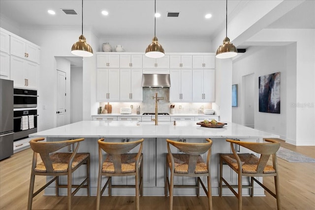 kitchen featuring tasteful backsplash, light countertops, visible vents, light wood-type flooring, and under cabinet range hood