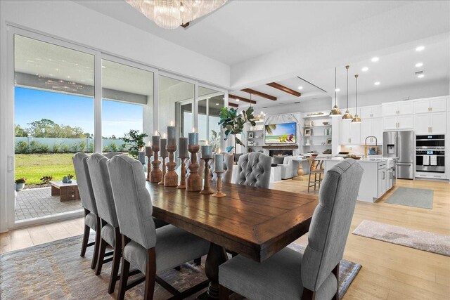 dining area with light wood finished floors, a warm lit fireplace, beam ceiling, and recessed lighting