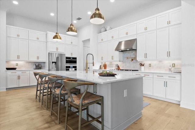 kitchen with stainless steel appliances, visible vents, wall chimney range hood, and light wood finished floors