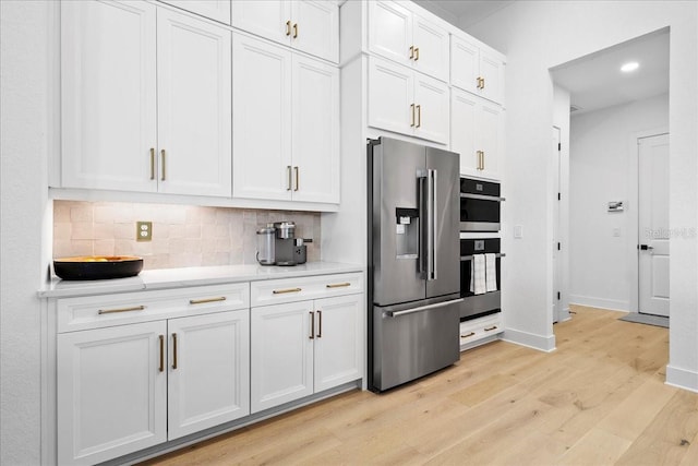 kitchen featuring backsplash, appliances with stainless steel finishes, white cabinets, light wood-type flooring, and baseboards