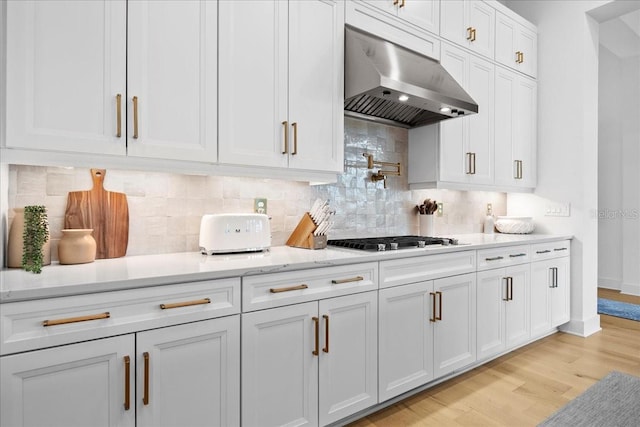 kitchen with gas cooktop, white cabinets, wall chimney range hood, light wood-type flooring, and tasteful backsplash