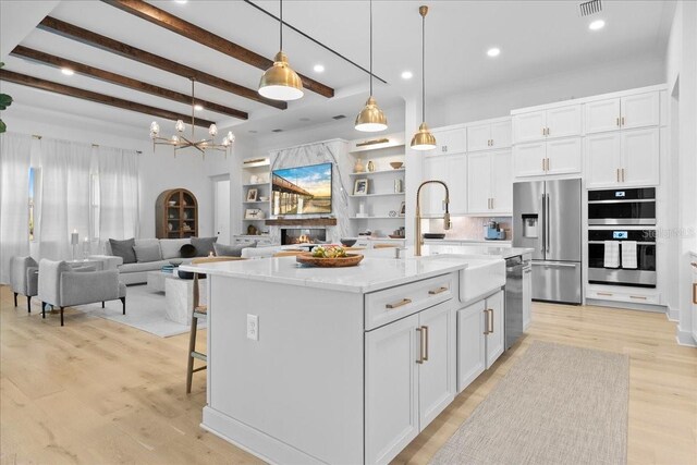 kitchen featuring decorative light fixtures, stainless steel appliances, light wood-style floors, a large fireplace, and white cabinets