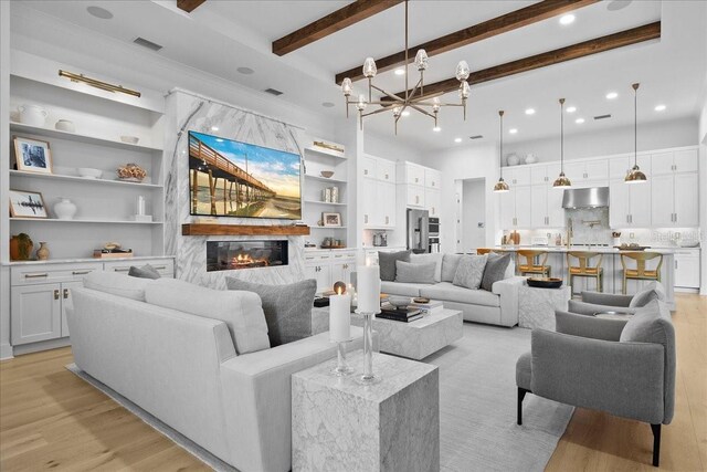 living area featuring a chandelier, light wood-type flooring, a large fireplace, and beamed ceiling