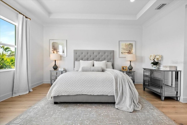 bedroom featuring baseboards, visible vents, a raised ceiling, and wood finished floors