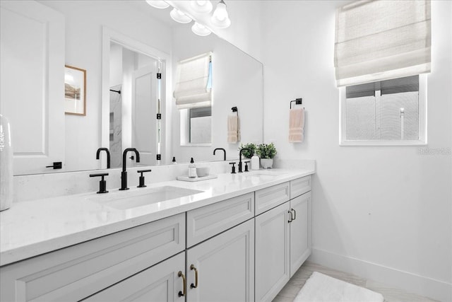 bathroom featuring double vanity, walk in shower, a sink, and baseboards