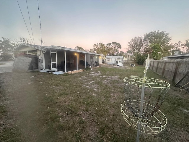 yard at dusk featuring fence and a sunroom